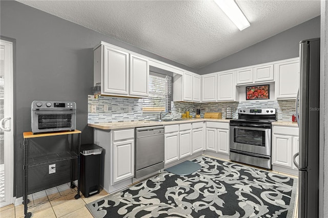 kitchen with white cabinetry, vaulted ceiling, light tile patterned floors, appliances with stainless steel finishes, and decorative backsplash