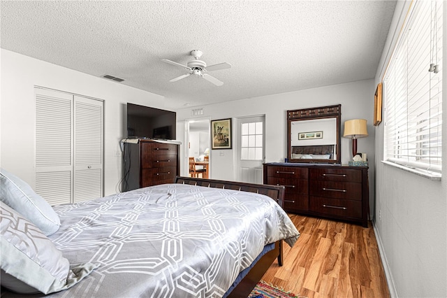 bedroom with light hardwood / wood-style flooring, a textured ceiling, ceiling fan, and a closet