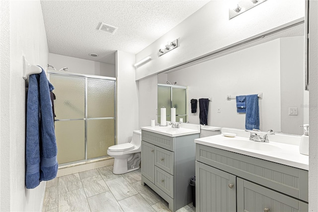 bathroom with vanity, toilet, a shower with shower door, and a textured ceiling