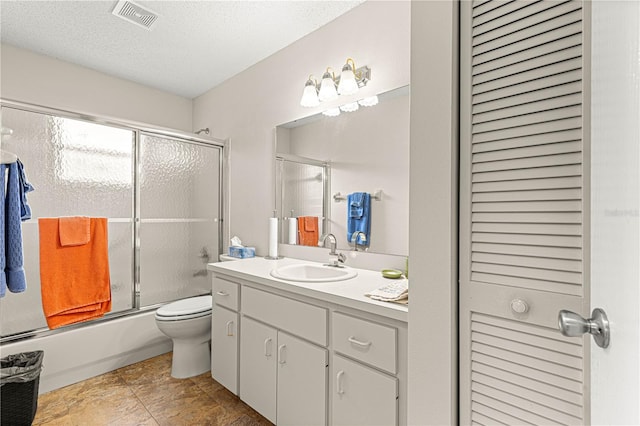 full bathroom with vanity, toilet, combined bath / shower with glass door, and a textured ceiling