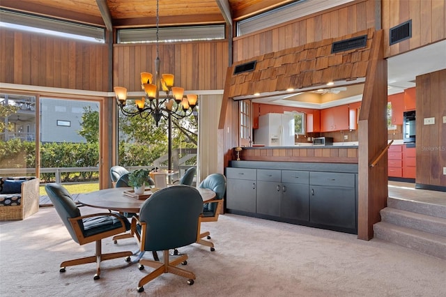 dining space with a notable chandelier, light colored carpet, a high ceiling, and wood walls