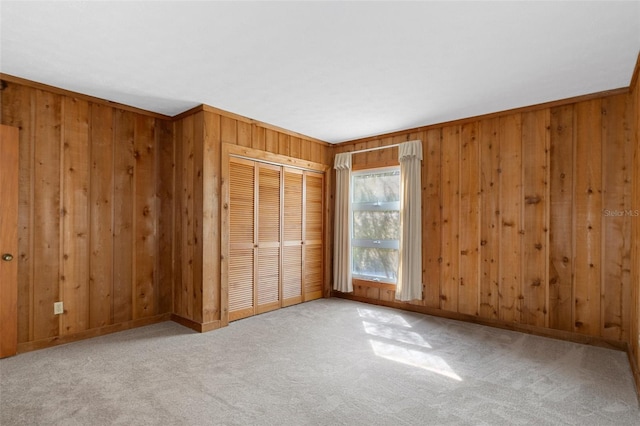 unfurnished bedroom featuring ornamental molding, light colored carpet, a closet, and wood walls