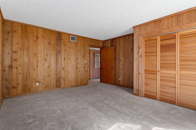 unfurnished bedroom with light colored carpet, a closet, and wood walls