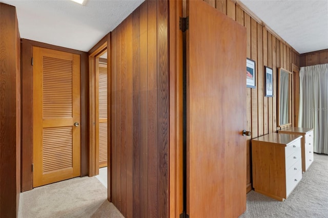 hallway with wooden walls, light carpet, and a textured ceiling