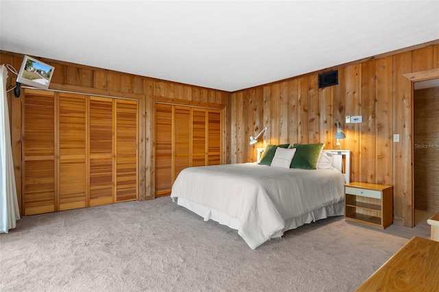 carpeted bedroom featuring two closets and wooden walls