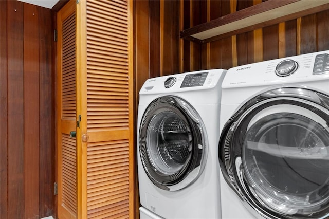 clothes washing area with washing machine and dryer and wood walls