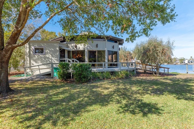 back of house with a deck with water view, a lawn, and a sunroom