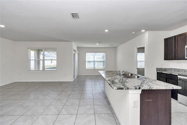 kitchen with a kitchen island with sink, sink, light stone counters, and a healthy amount of sunlight