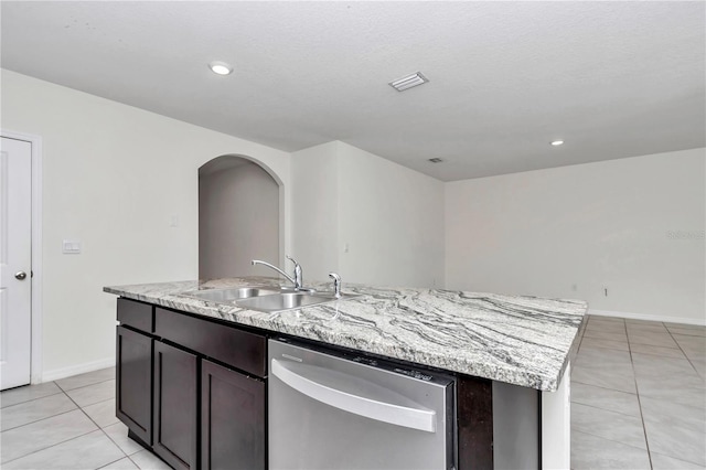 kitchen featuring light tile patterned flooring, dark brown cabinetry, sink, stainless steel dishwasher, and an island with sink