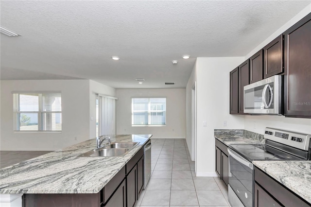 kitchen with sink, a textured ceiling, light tile patterned floors, stainless steel appliances, and a kitchen island with sink