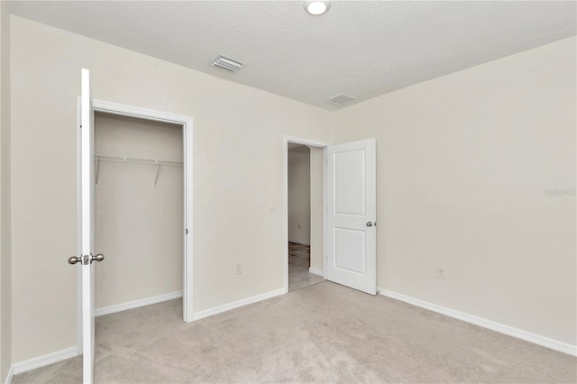 unfurnished bedroom featuring light colored carpet, a textured ceiling, and a closet