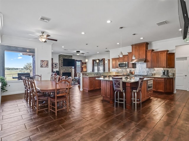 kitchen featuring light stone counters, a center island, hanging light fixtures, ornamental molding, and a kitchen breakfast bar