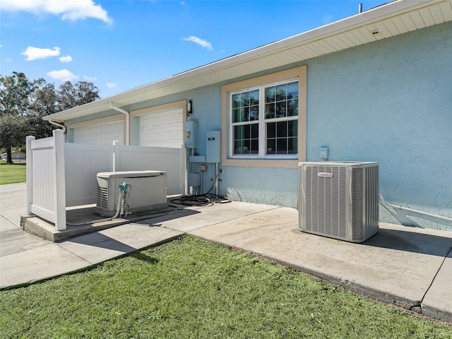 view of exterior entry featuring a garage, a lawn, and central air condition unit