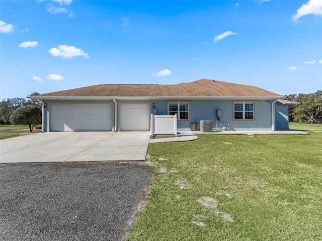 ranch-style home featuring an attached garage, central air condition unit, concrete driveway, stucco siding, and a front lawn