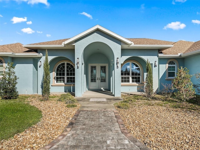 view of exterior entry with stucco siding, a shingled roof, and french doors