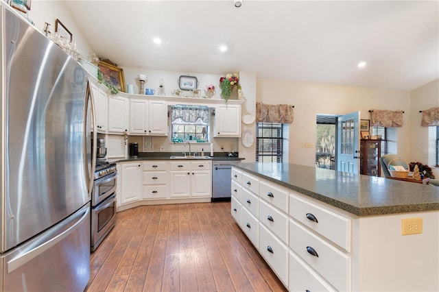 kitchen with sink, white cabinetry, hardwood / wood-style floors, stainless steel appliances, and a kitchen island