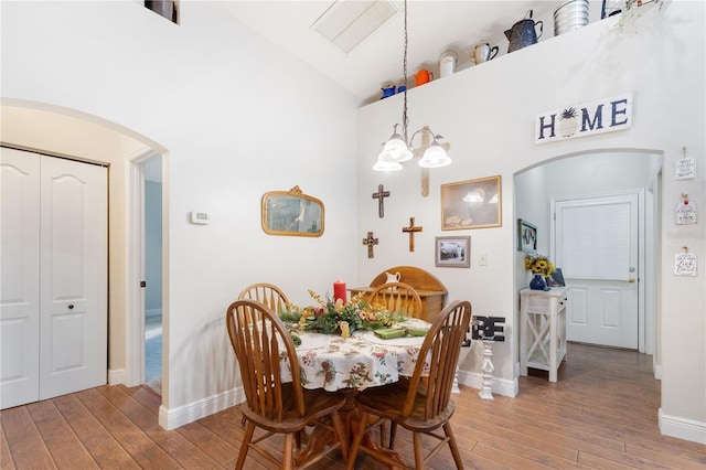 dining area with an inviting chandelier, wood-type flooring, and high vaulted ceiling