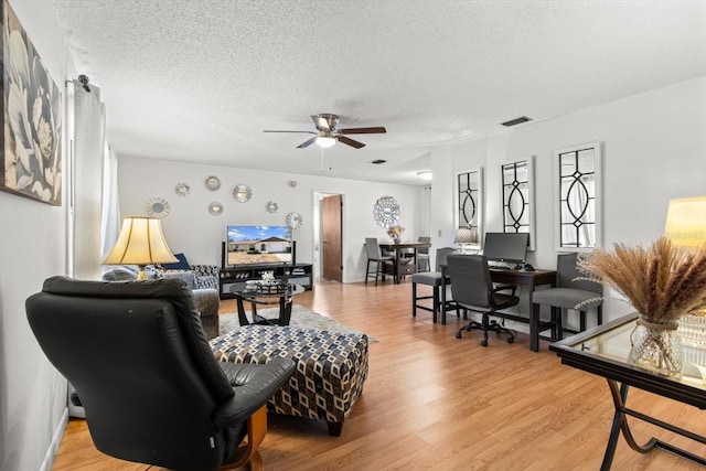 living room with ceiling fan, light hardwood / wood-style floors, and a textured ceiling