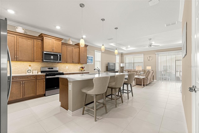 kitchen featuring a kitchen bar, crown molding, decorative light fixtures, a center island with sink, and appliances with stainless steel finishes