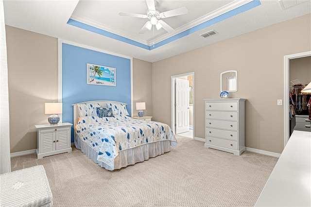 carpeted bedroom featuring ornamental molding, a walk in closet, ceiling fan, a tray ceiling, and a closet