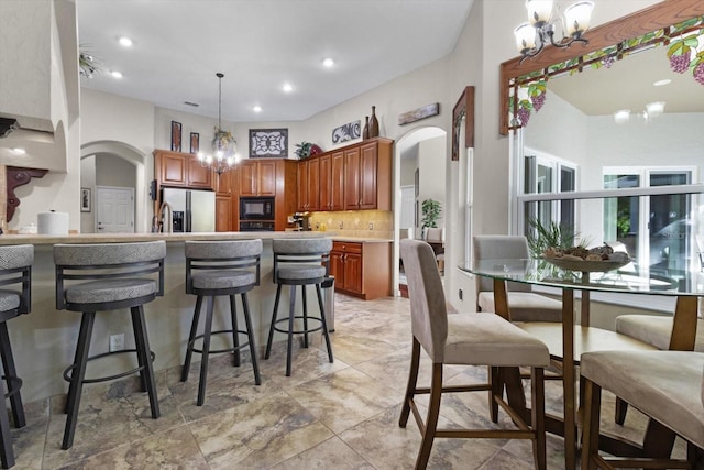 kitchen with decorative backsplash, stainless steel fridge, black microwave, and a chandelier