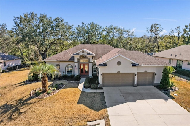 mediterranean / spanish-style house with a garage, french doors, and a front lawn