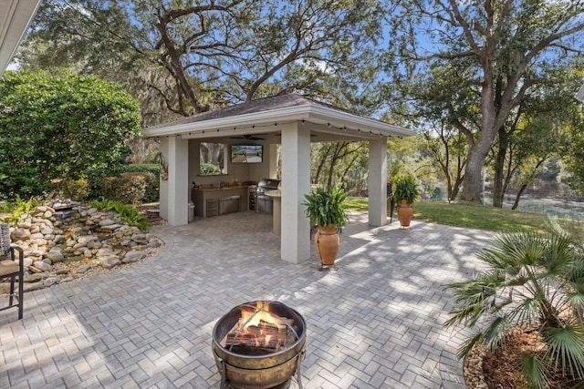 view of patio featuring a gazebo, a grill, exterior kitchen, and a fire pit