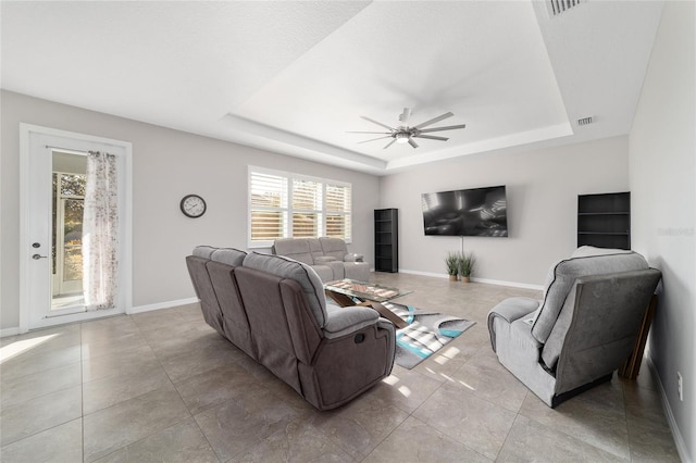 tiled living room with a tray ceiling and ceiling fan