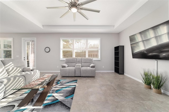 tiled living room with a raised ceiling and ceiling fan