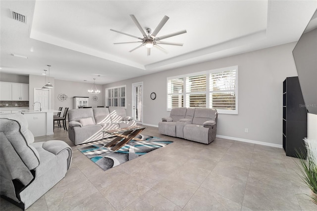 living room with sink, a tray ceiling, and ceiling fan with notable chandelier