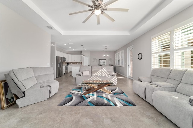 living room with ceiling fan with notable chandelier and a tray ceiling