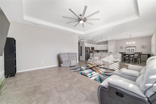 living room with a raised ceiling and ceiling fan with notable chandelier