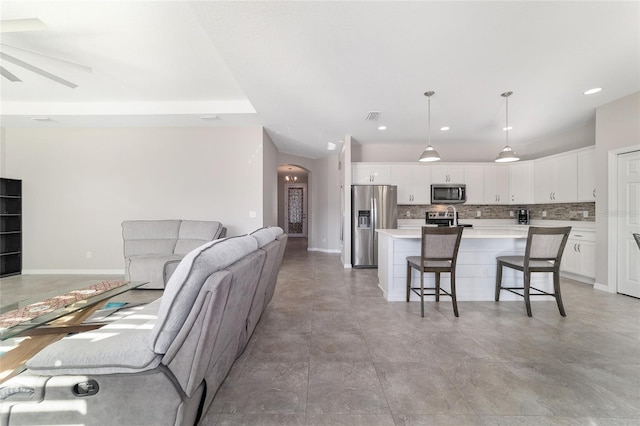 kitchen featuring appliances with stainless steel finishes, pendant lighting, white cabinetry, a breakfast bar area, and a kitchen island with sink