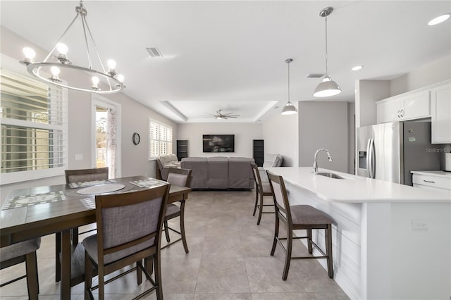 dining area with sink, ceiling fan with notable chandelier, light tile patterned floors, and a tray ceiling