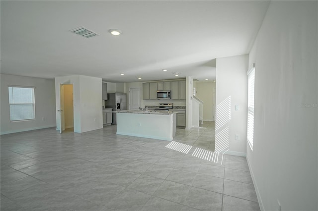 kitchen featuring visible vents, open floor plan, an island with sink, gray cabinets, and appliances with stainless steel finishes