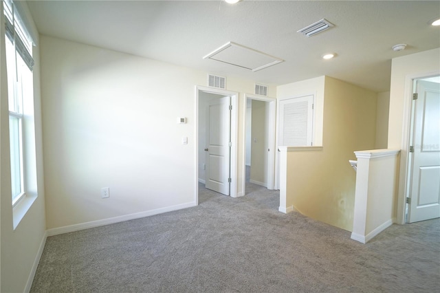 carpeted spare room featuring visible vents, baseboards, and attic access