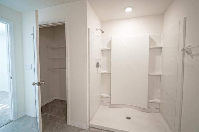 full bath with tile patterned floors, a spacious closet, baseboards, and a stall shower