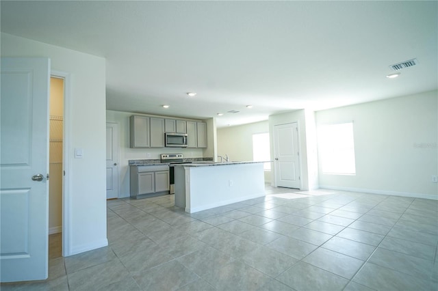 kitchen with visible vents, gray cabinetry, a center island with sink, stainless steel appliances, and light tile patterned flooring