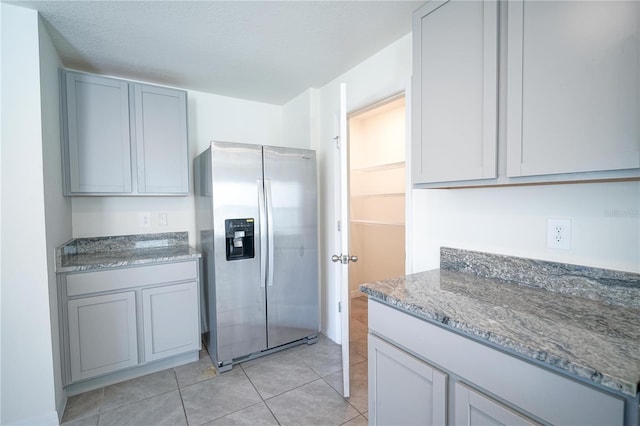 kitchen with light tile patterned floors, stone counters, a textured ceiling, and stainless steel refrigerator with ice dispenser