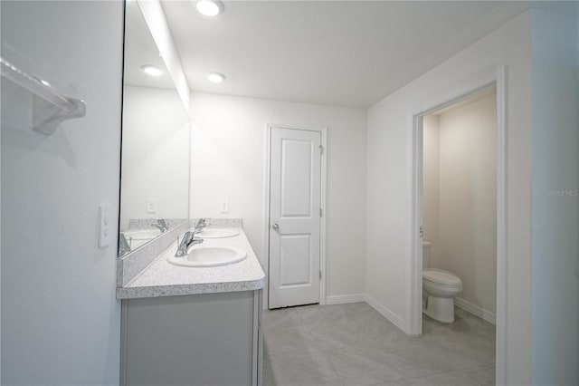 bathroom with double vanity, toilet, baseboards, and a sink