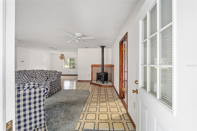 living room featuring ceiling fan, a wood stove, and a textured ceiling