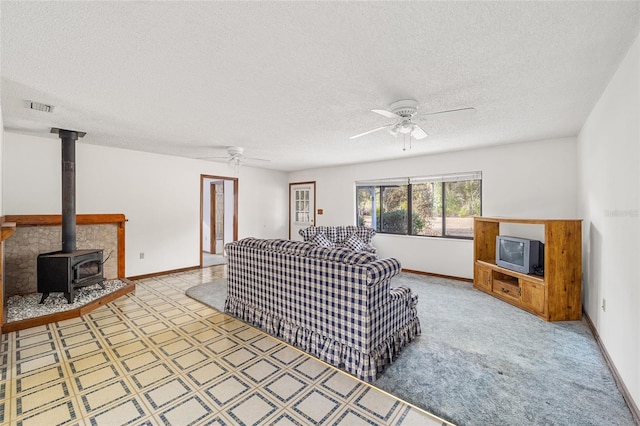 living room with ceiling fan, carpet floors, a textured ceiling, and a wood stove