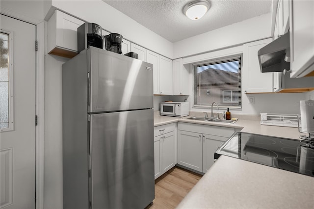 kitchen with a textured ceiling, extractor fan, a sink, light countertops, and appliances with stainless steel finishes