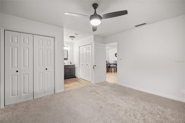 unfurnished bedroom featuring a textured ceiling, ensuite bathroom, light colored carpet, visible vents, and multiple closets