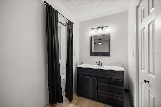 bathroom with a textured ceiling, toilet, wood finished floors, and vanity