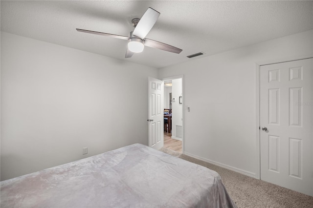 bedroom featuring light carpet, a textured ceiling, visible vents, and baseboards