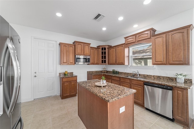 kitchen with sink, a center island, light tile patterned floors, appliances with stainless steel finishes, and dark stone counters