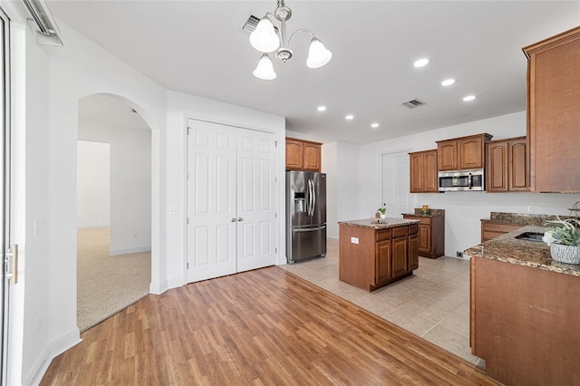 kitchen featuring a center island, light wood-type flooring, appliances with stainless steel finishes, pendant lighting, and light stone countertops