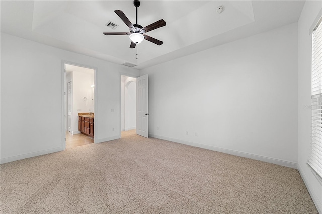 unfurnished bedroom with ceiling fan, light colored carpet, ensuite bathroom, and a raised ceiling