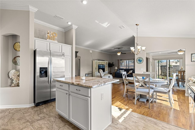 kitchen featuring lofted ceiling, white cabinetry, decorative light fixtures, stainless steel fridge, and a kitchen island